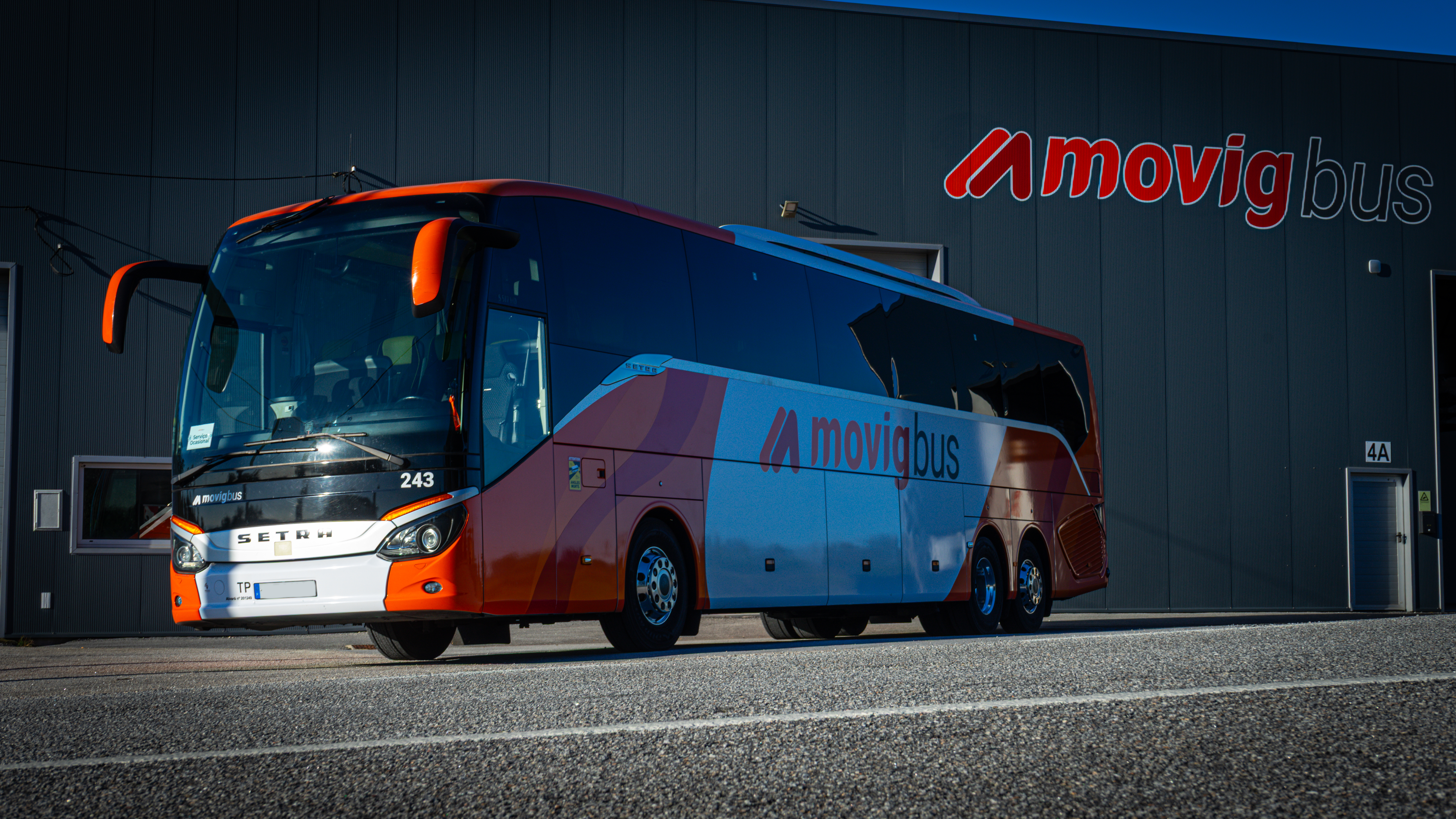 Autocarro MOVIG diante de um edifício com a identificação da empresa